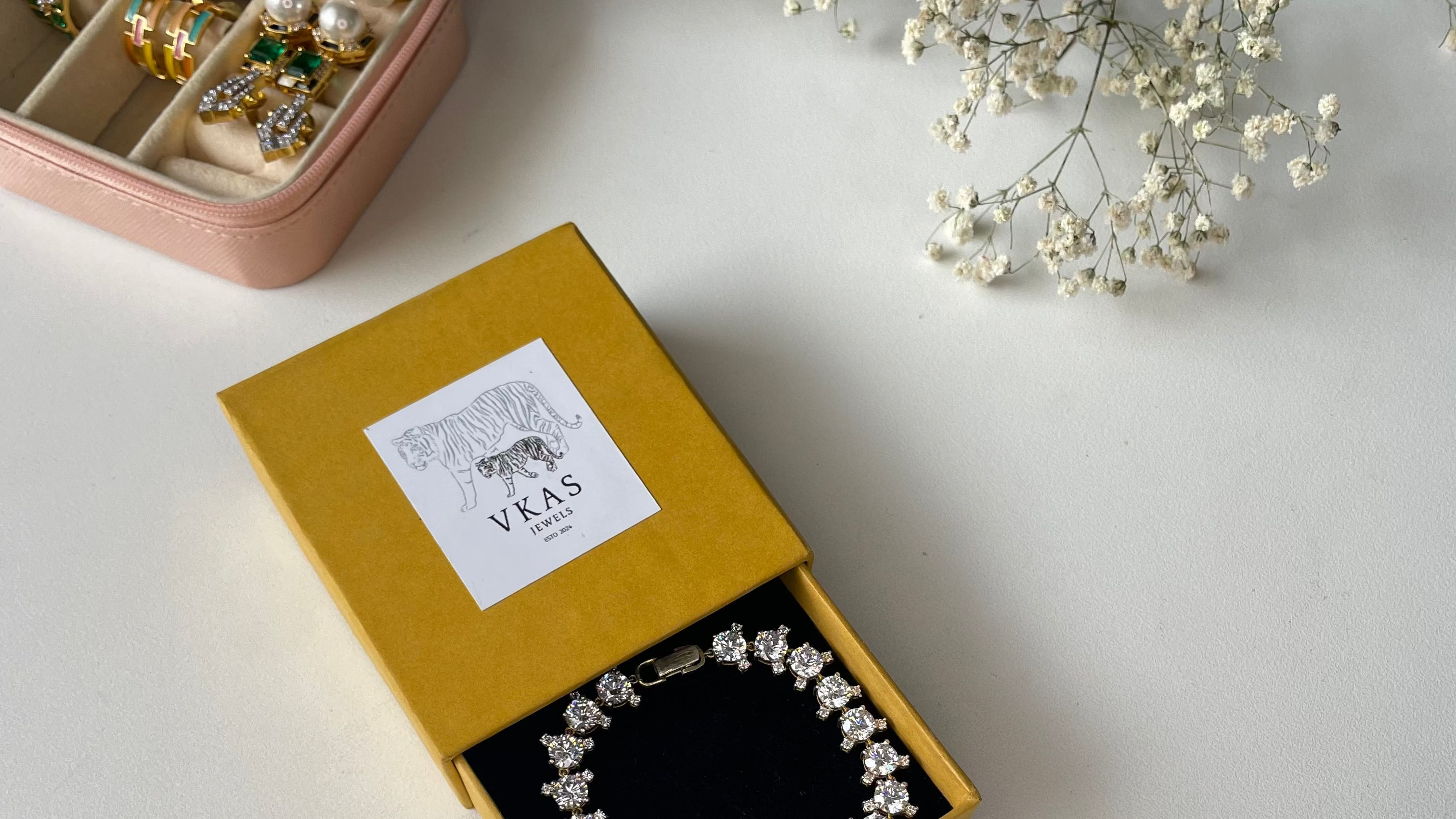 Jewelry box with a necklace inside, branded 'VKAS', on a light surface with flowers.